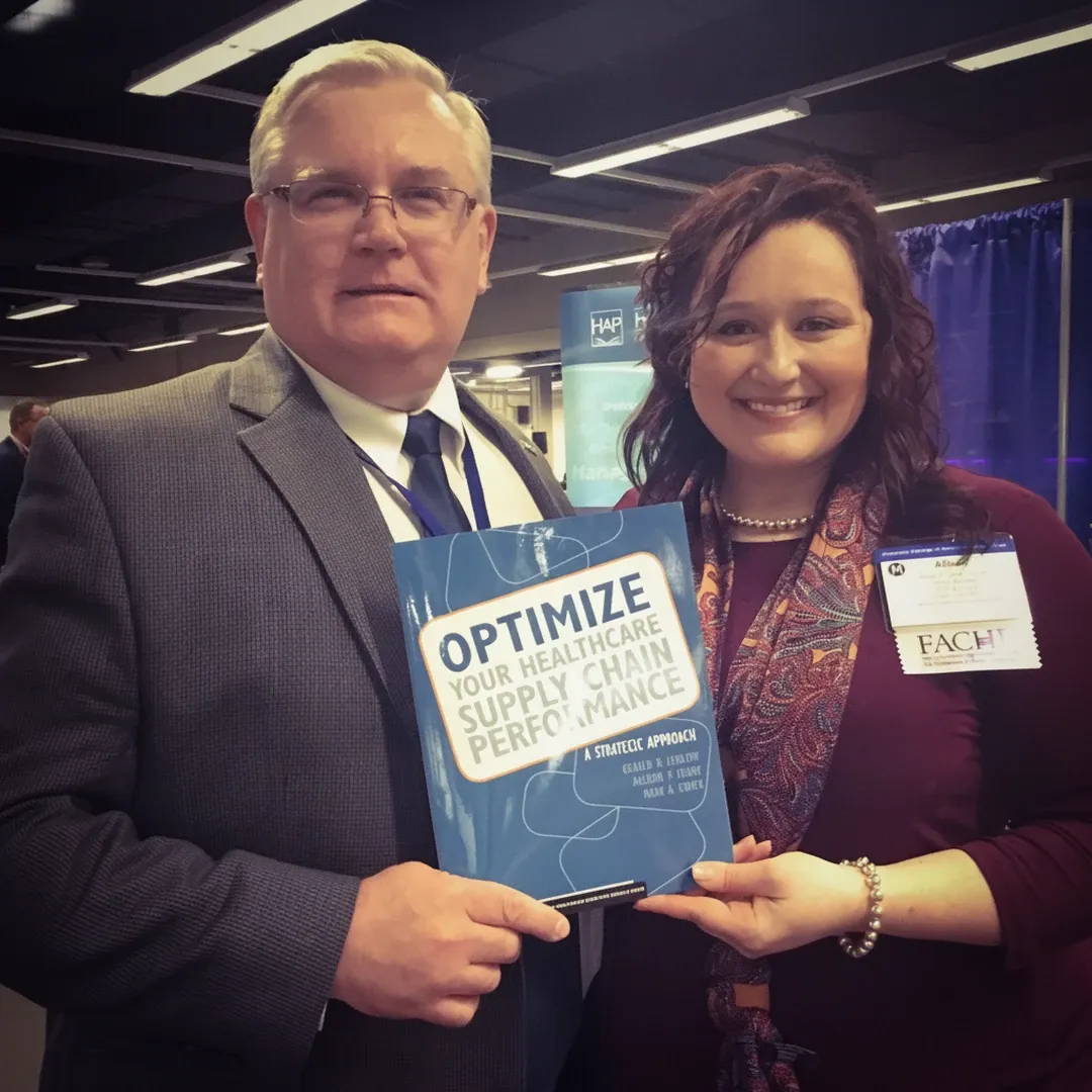 Allison Corry and co-author Gerald “Jerry” Ledlow holding a copy of Optimize Your Healthcare Supply Chain Performance at a healthcare conference