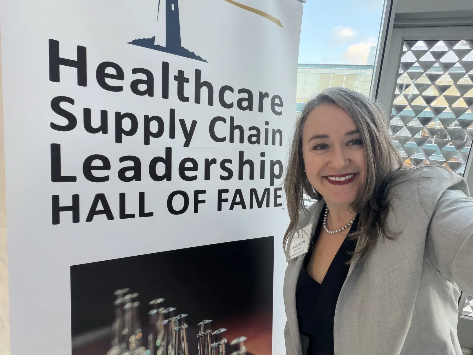 Allison Corry beside the Healthcare Supply Chain Leadership Hall of Fame banner