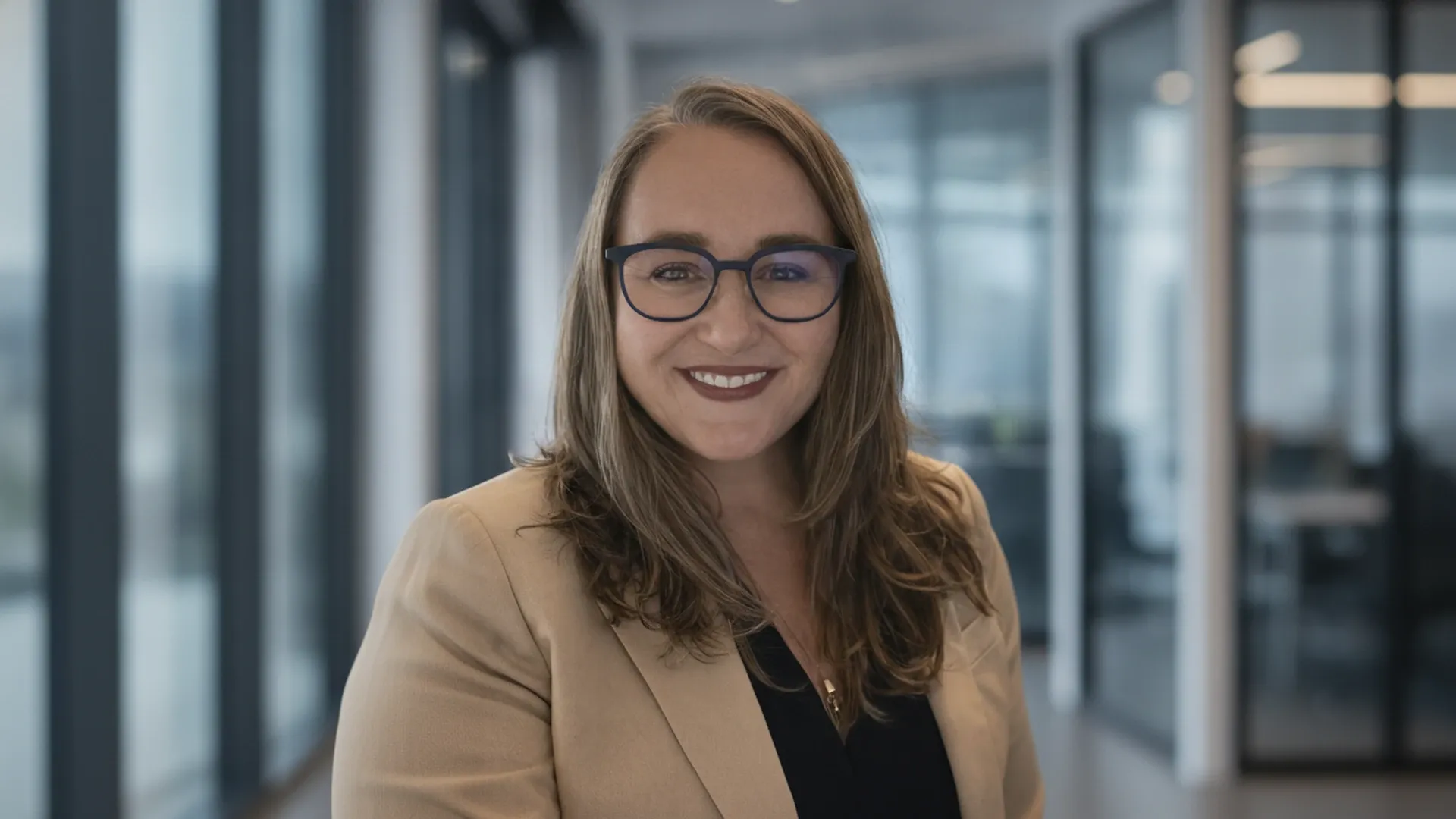 Allison P. Corry smiling in a glass-walled office corridor